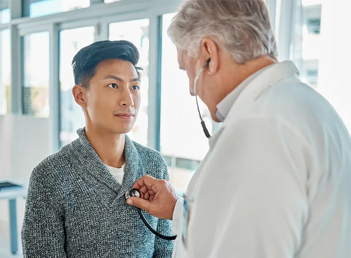 Doctor using a stethoscope to examine a male patient’s chest during a medical checkup in a clinical setting.