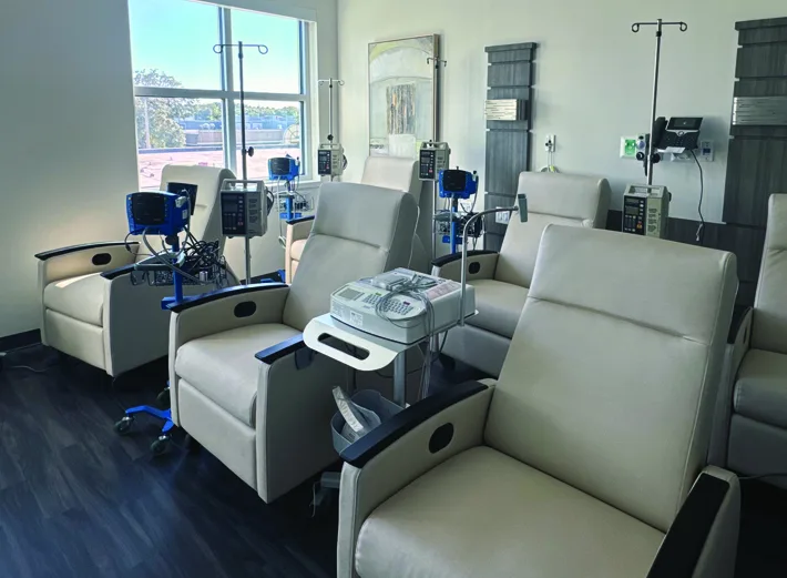 Modern medical infusion room with multiple reclining treatment chairs, IV poles, and infusion pumps arranged in a clean, well lit clinical space.