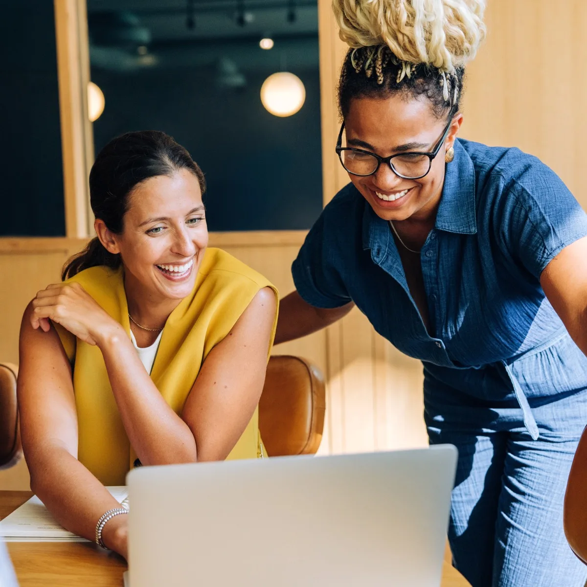 Two adult women enjoying a productive work environment, actively engaging and collaborating over a laptop.